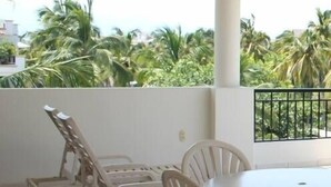 A balcony with a table and chairs, a ceiling fan, and a view of palm trees.