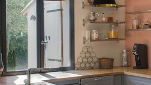 A modern kitchen with a white sink, wooden countertop, hanging pendant lights, and a view of a house through a glass door. - Villa des jacinthes (Tarascon)