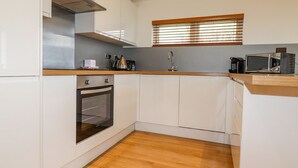 Eine kleine Küche mit weißen Schränken, einem eingebauten Backofen, einer Mikrowelle und einem Fenster mit Jalousien.