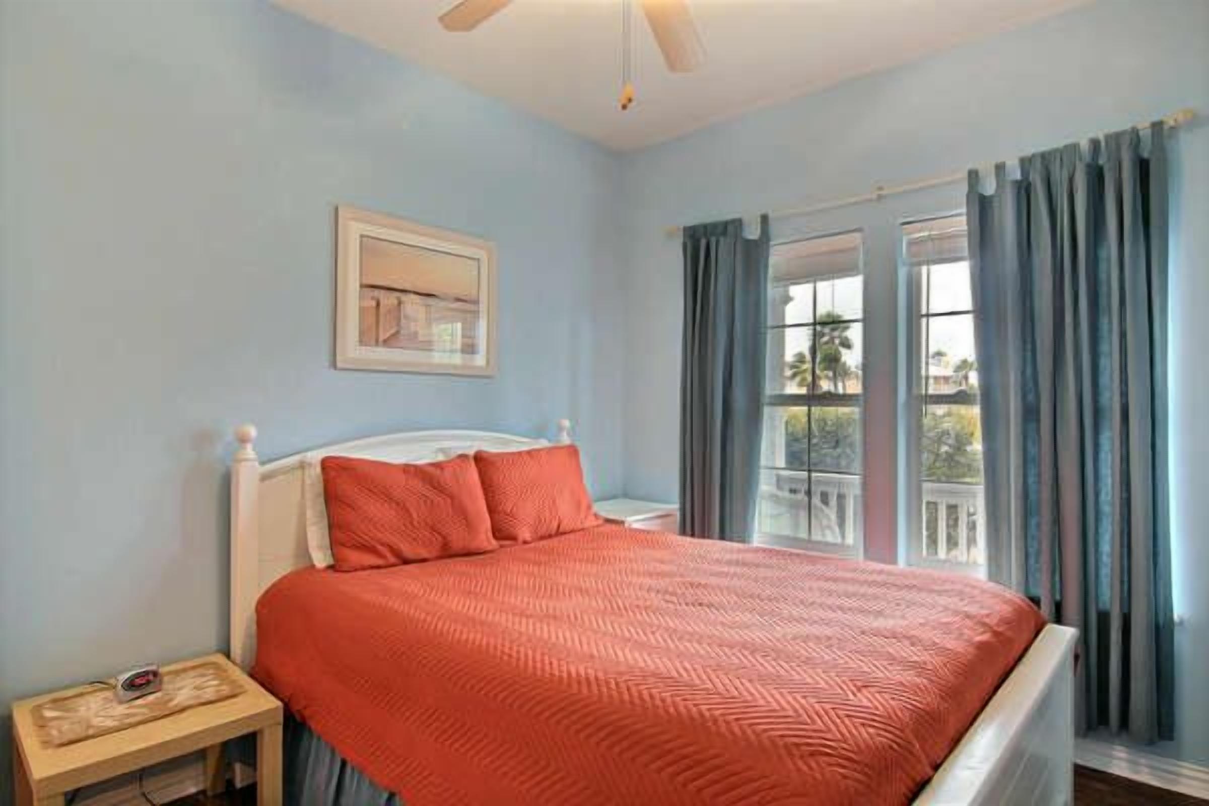A bedroom with a bed, a nightstand, a ceiling fan, and a window with curtains.