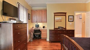 A bedroom with a bed, a desk with a computer, a TV, and wooden furniture.