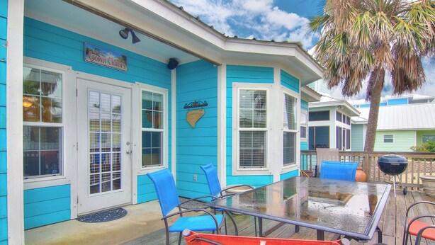 A turquoise house with a glass table and chairs, a palm tree, and a sign that reads "Welcome to Coconut Charles."