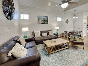 A living room with a brown leather sofa, two side tables with lamps, a wooden coffee table, and a painting on the wall. - Dock Holiday by Silver Sands Vacation Rentals (Port Aransas)