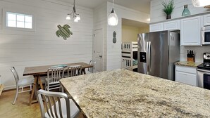 A modern kitchen with white cabinetry, a granite countertop, stainless steel appliances, and a dining area with white chairs.