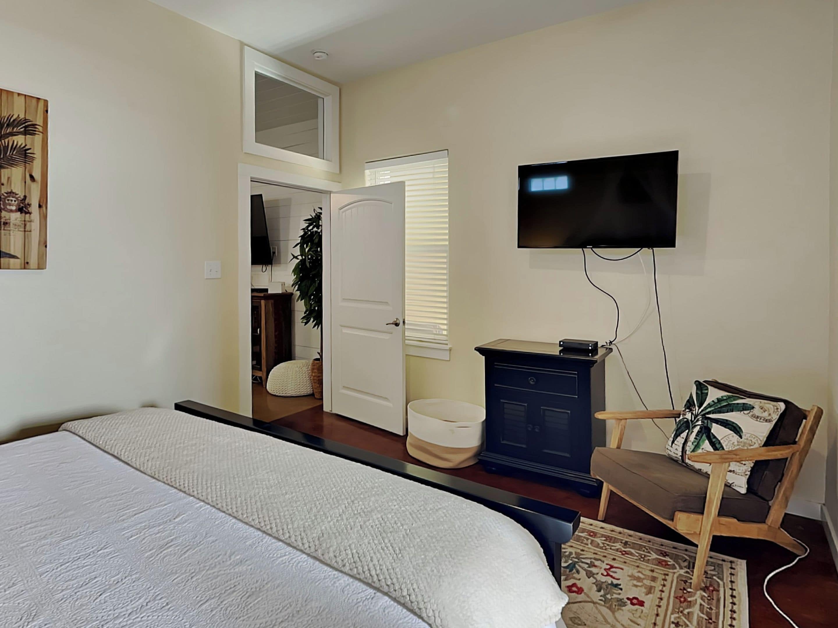 A bedroom with a bed, a TV mounted on the wall, a desk with a computer, and a chair.