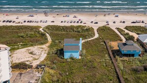A beachside property with a parking area, a pathway leading to a blue building, and a view of the ocean. - Crandall's Cottage by Silver Sands Vacation Rentals (Port Aransas)