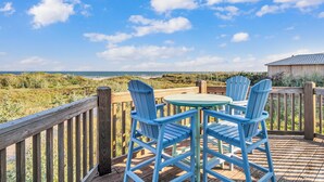 A wooden deck with blue chairs and a table overlooking a beach. - Crandall's Cottage by Silver Sands Vacation Rentals (Port Aransas)