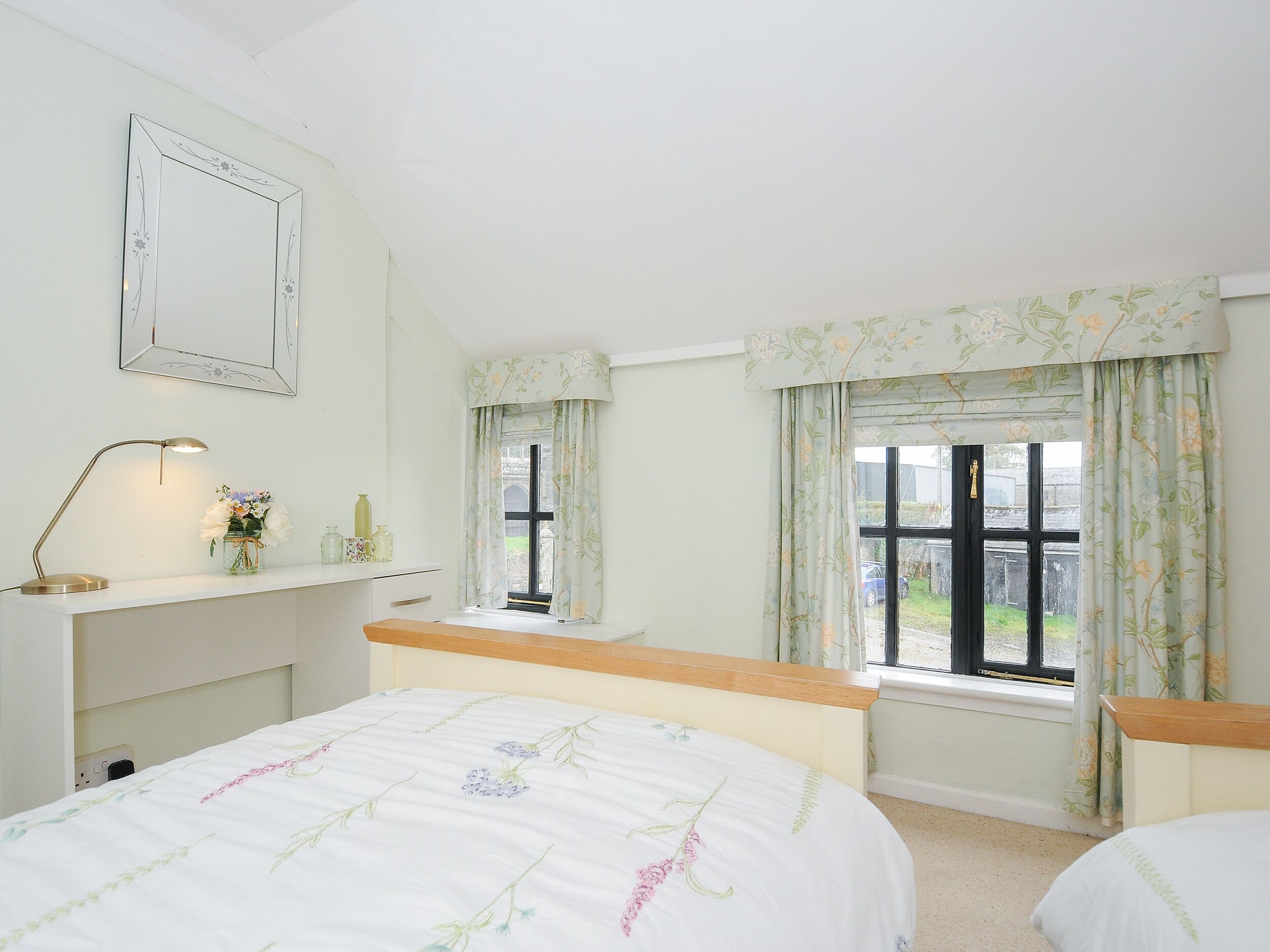 A bedroom with a bed, a bedside table, a lamp, a mirror, and a window with curtains.