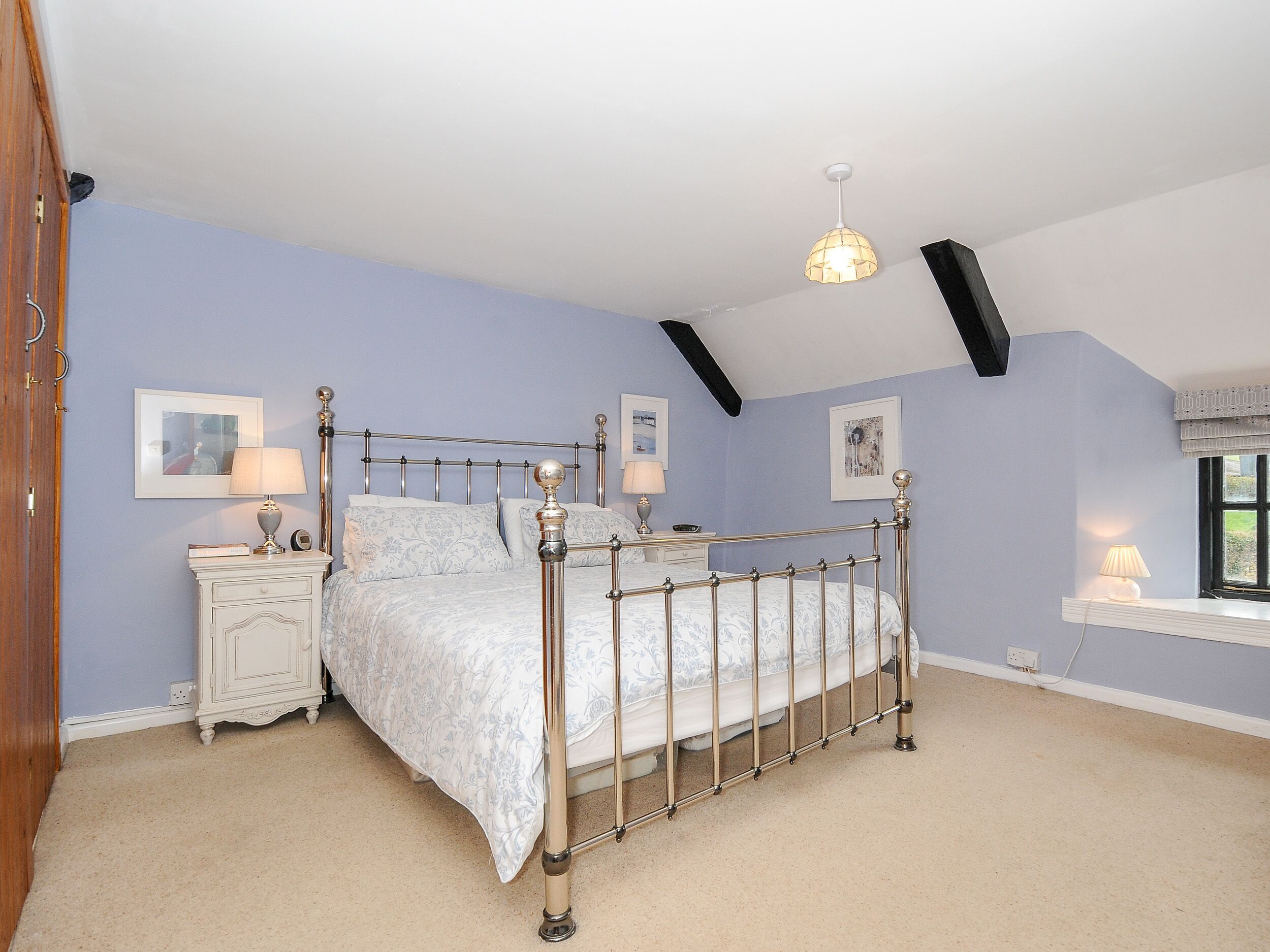 A bedroom with a four-poster bed, a nightstand, a lamp, and a window with a view.