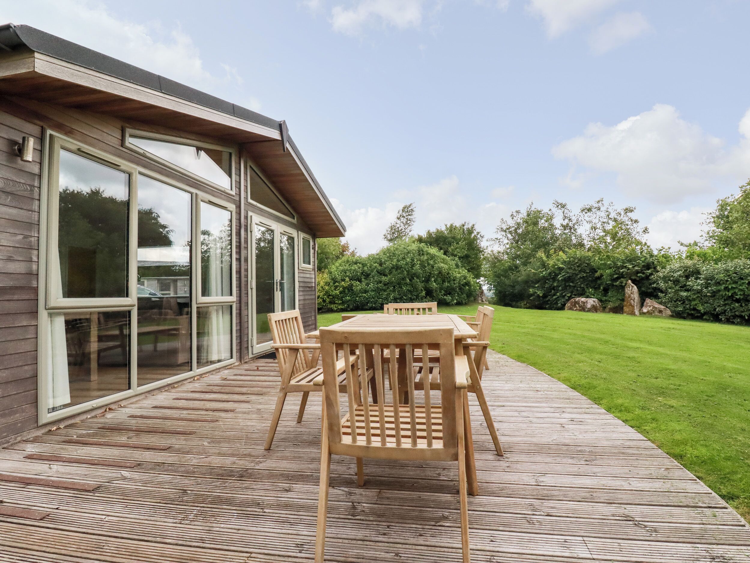 A wooden deck with a table and chairs, a glass door entrance, and a well-maintained lawn.