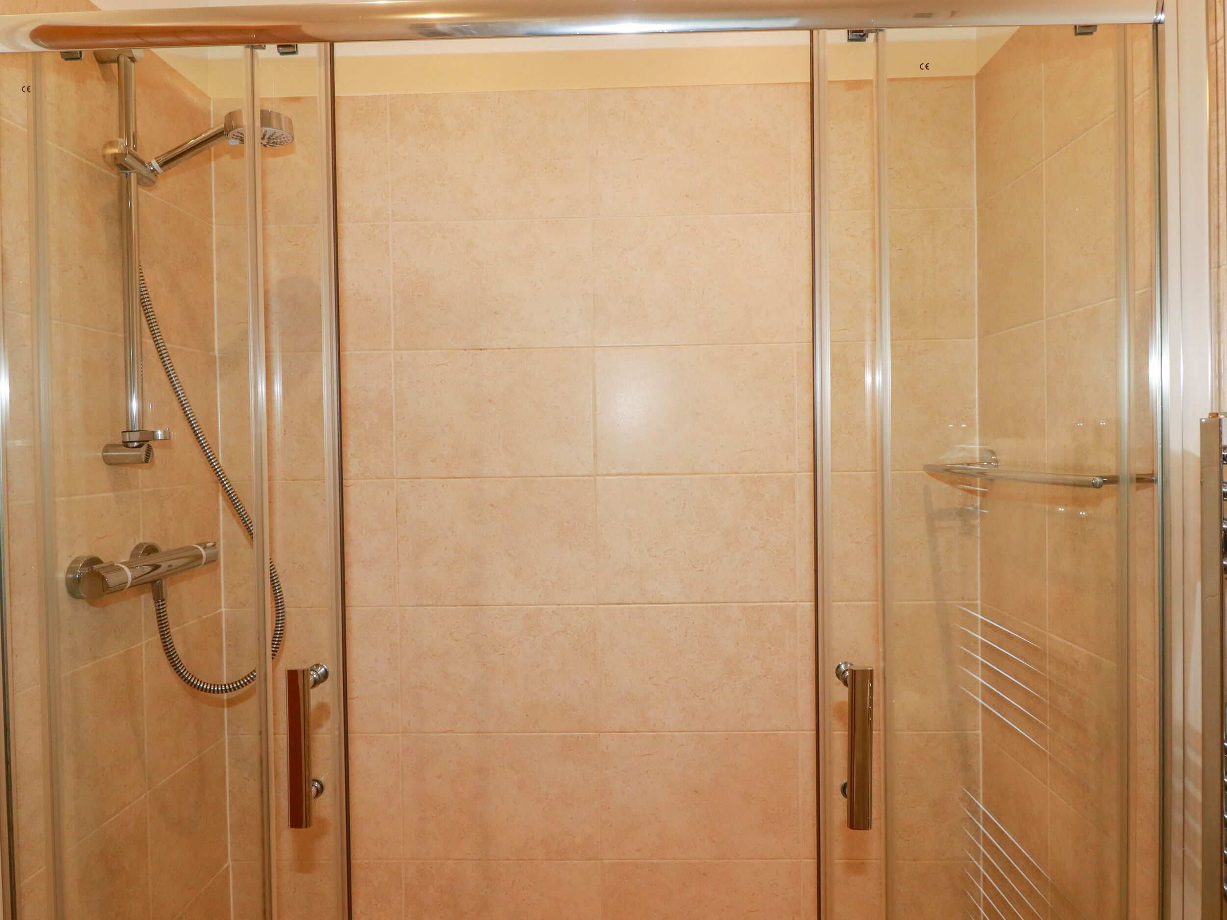 A glass-enclosed shower stall with a handheld showerhead and a handheld shower attachment.