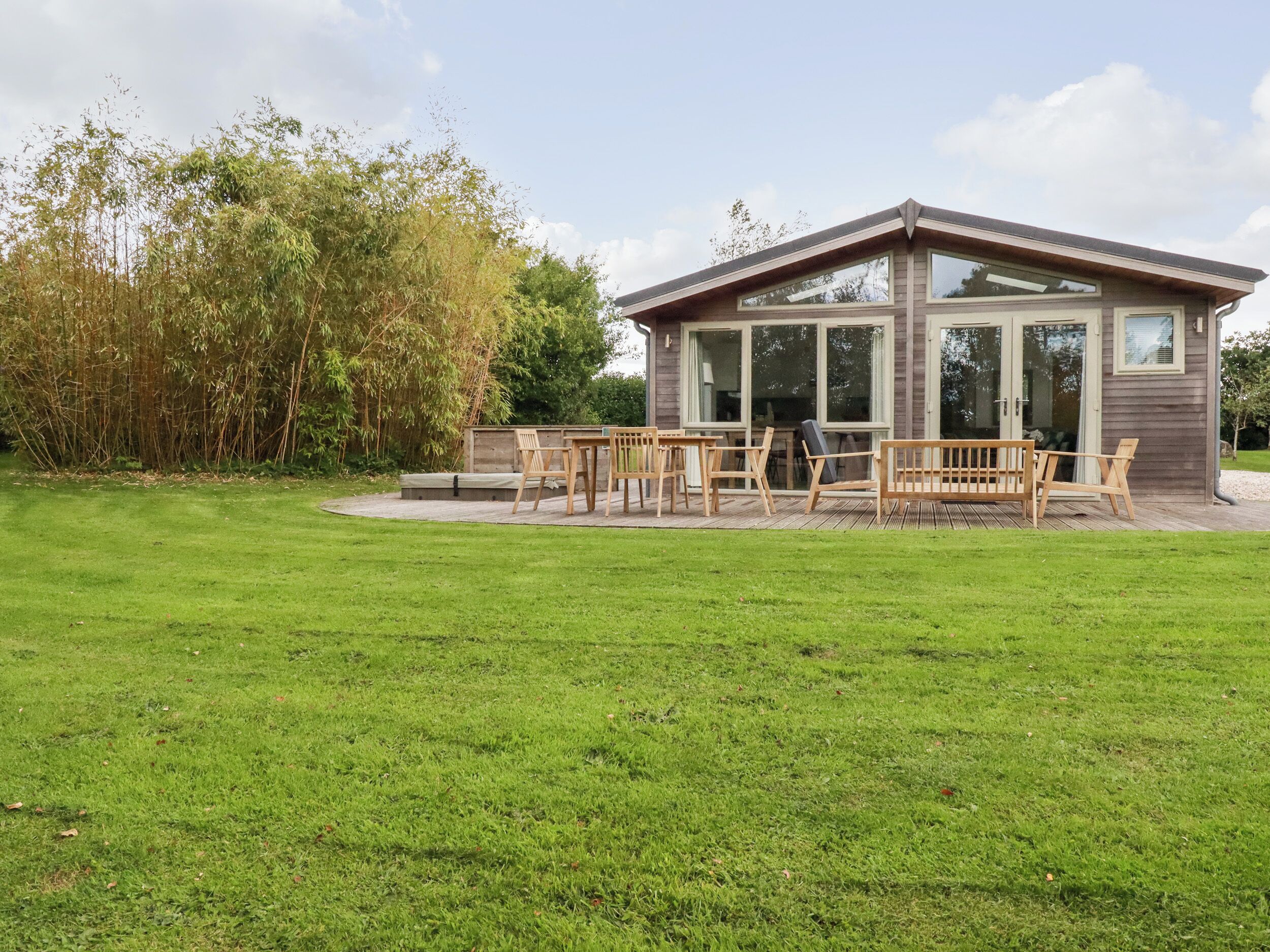 A modern house with a patio area featuring wooden furniture and a glass door leading to the interior.