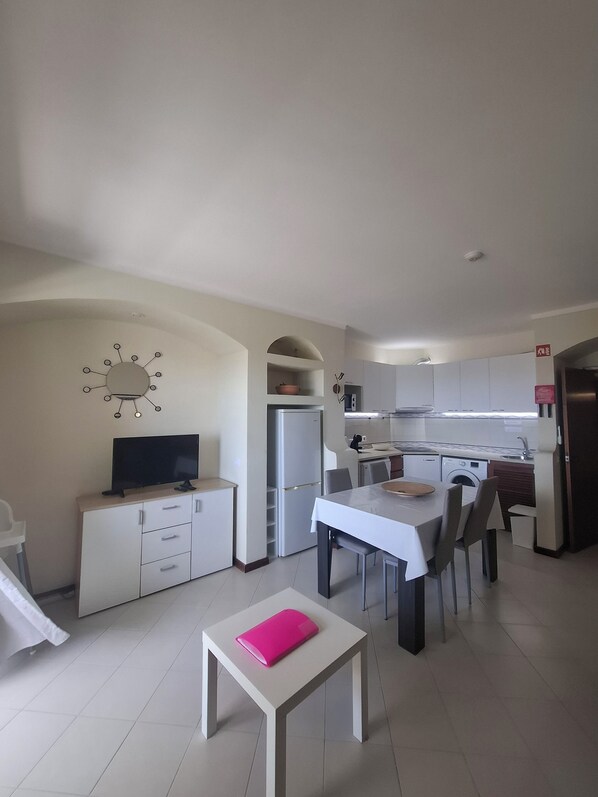 A modern kitchen with a dining area, a flat-screen TV, and a small table with a pink folder.