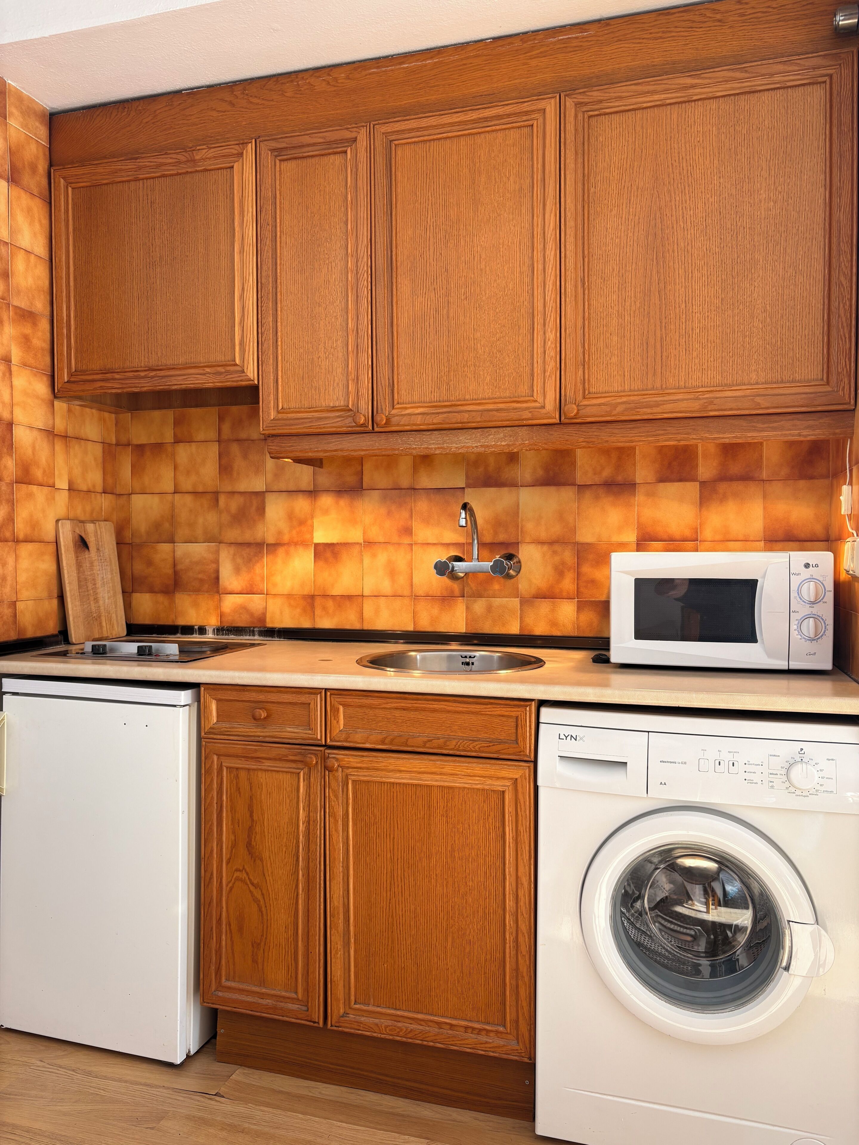 Cucina con mobili in legno, forno a microonde, lavello, lavastoviglie e lavatrice.