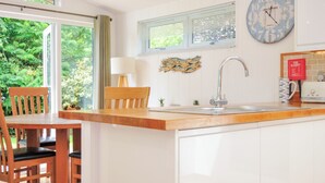A modern kitchen with a wooden island, white cabinetry, a built-in sink, and a large wall clock. - 15 Horizon View (Liskeard)