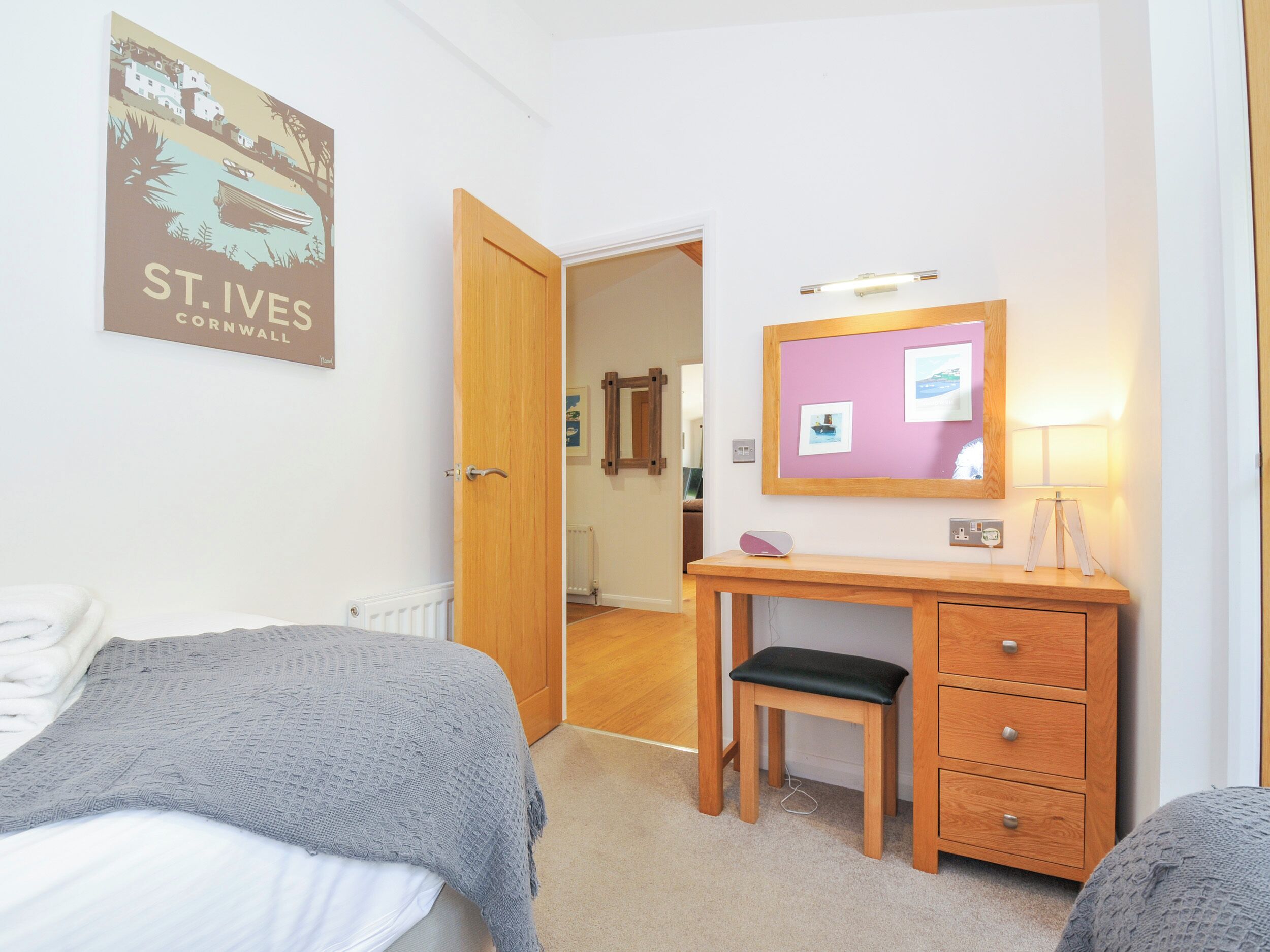 Een slaapkamer met een bed, een bureau met stoel, een dressoir, een spiegel en een ingelijste foto aan de muur.