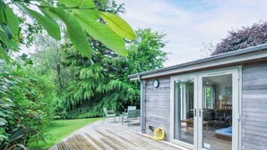 A wooden deck with a hot tub, a covered patio area with chairs, and a view of a lush garden. - 15 Horizon View (Liskeard)