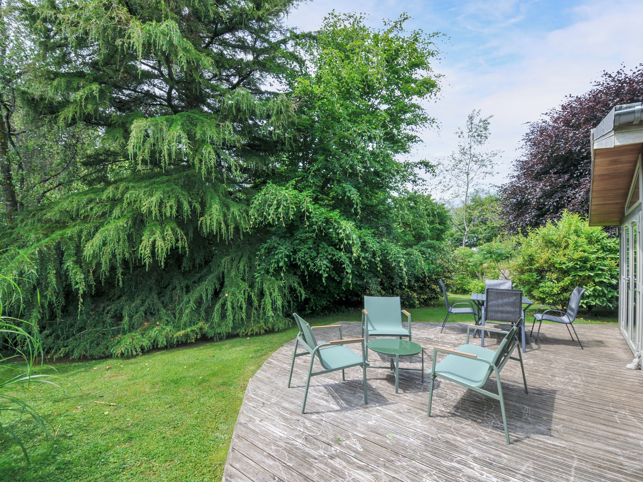A wooden deck with outdoor furniture, surrounded by lush greenery and trees.