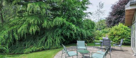 A wooden deck with outdoor furniture, surrounded by lush greenery and trees.
