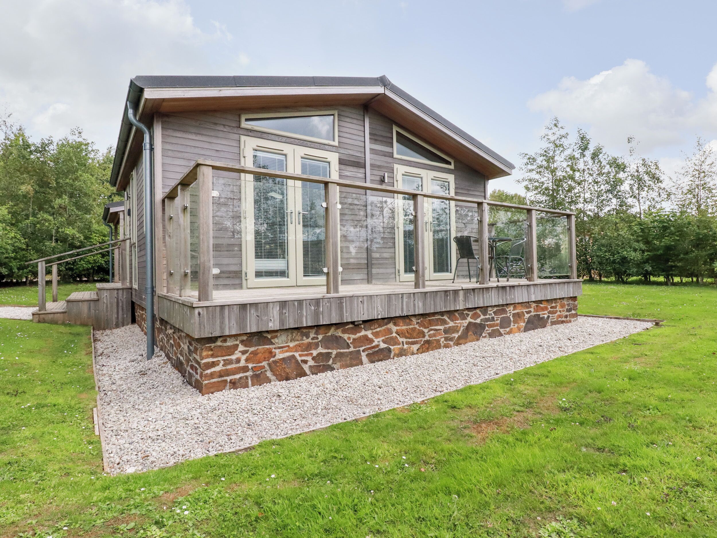 A modern house with a stone foundation, large windows, and a wooden deck.