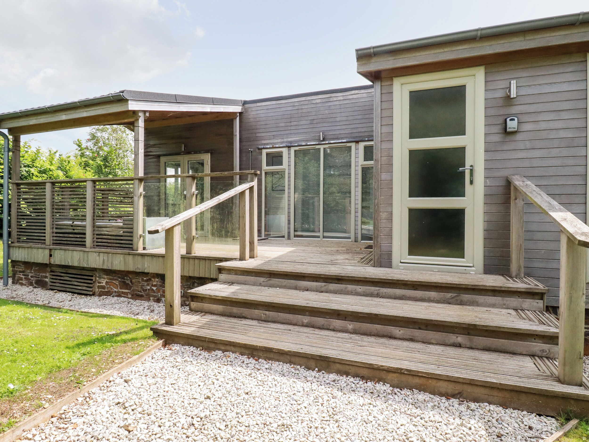 A modern house with a covered patio, a wooden deck, and a stone foundation.