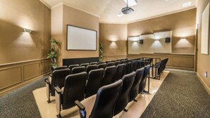 Uma sala de conferências com fileiras de cadeiras, uma tela de projetor e iluminação embutida nas paredes.
