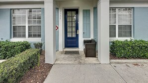 Uma entrada de edifício com porta azul, um pequeno alpendre e uma caixa de correio.