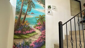 Eine Treppe mit beigen Fliesen, einem schwarzen Metallgeländer und einem großen Gemälde mit tropischer Landschaft an der Wand.