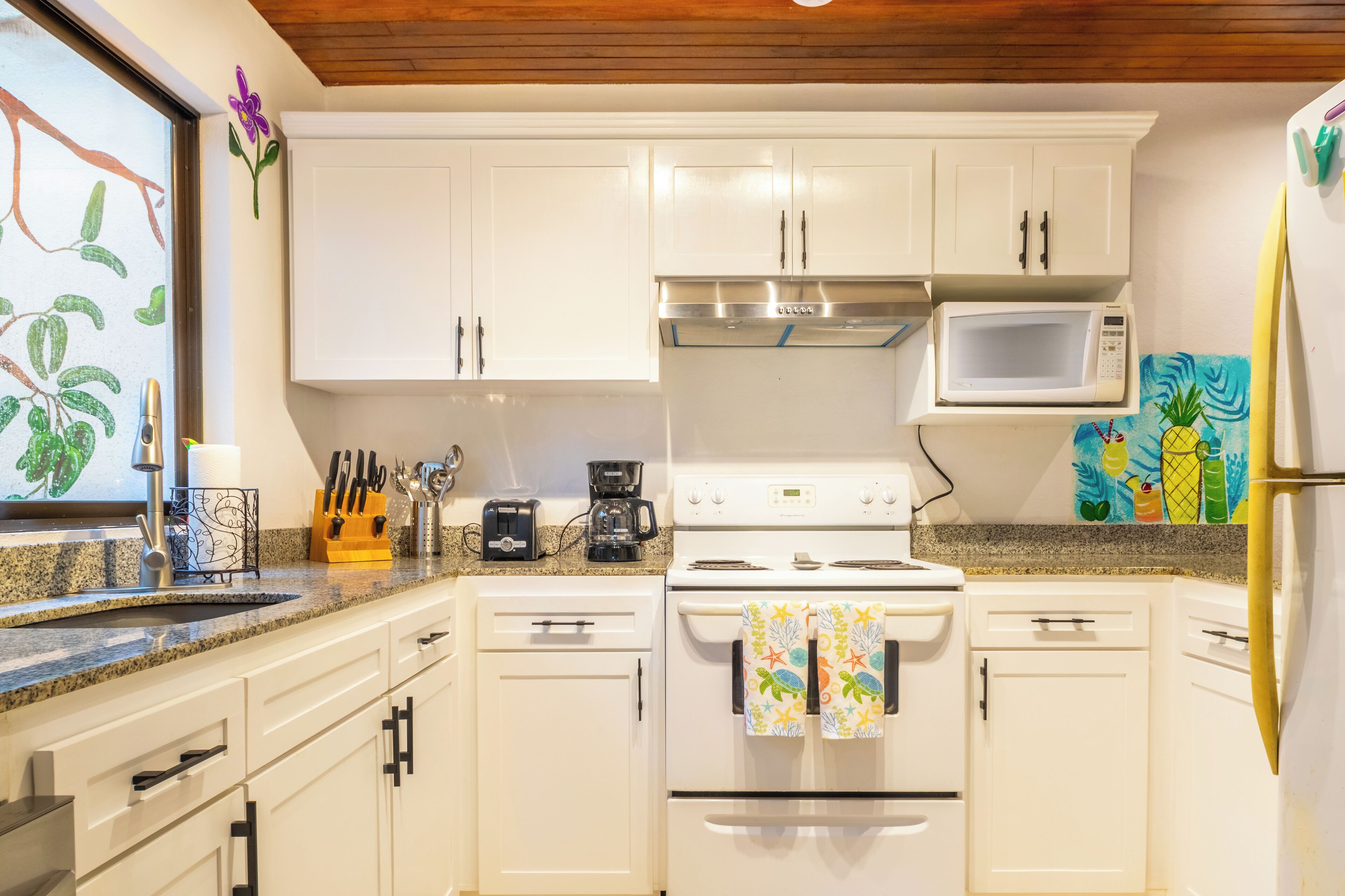 Una cocina con gabinetes blancos, una campana extractora de acero inoxidable, un microondas y un cuadro llamativo en la pared.