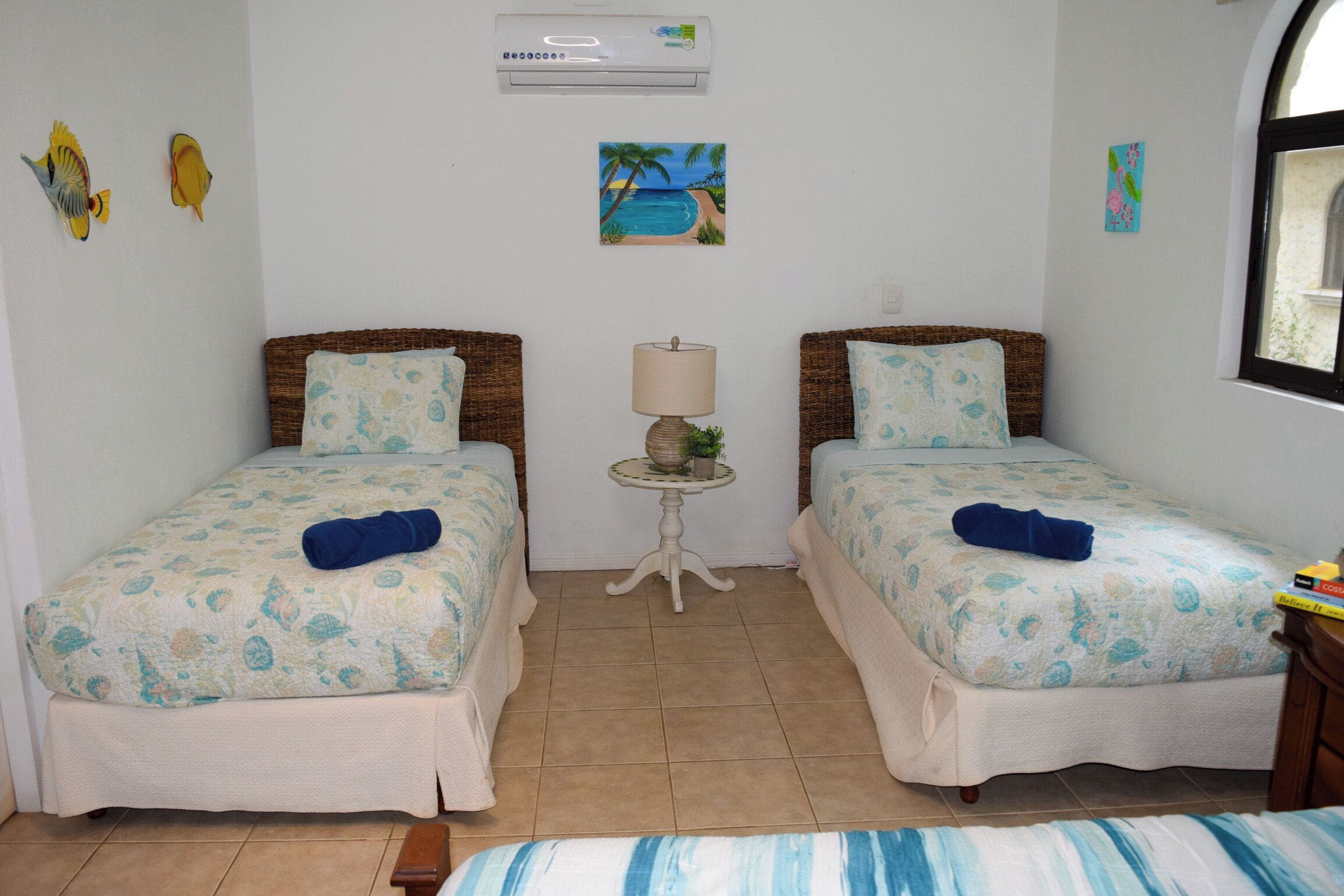 A room with two beds, a small table with a lamp, and a window.