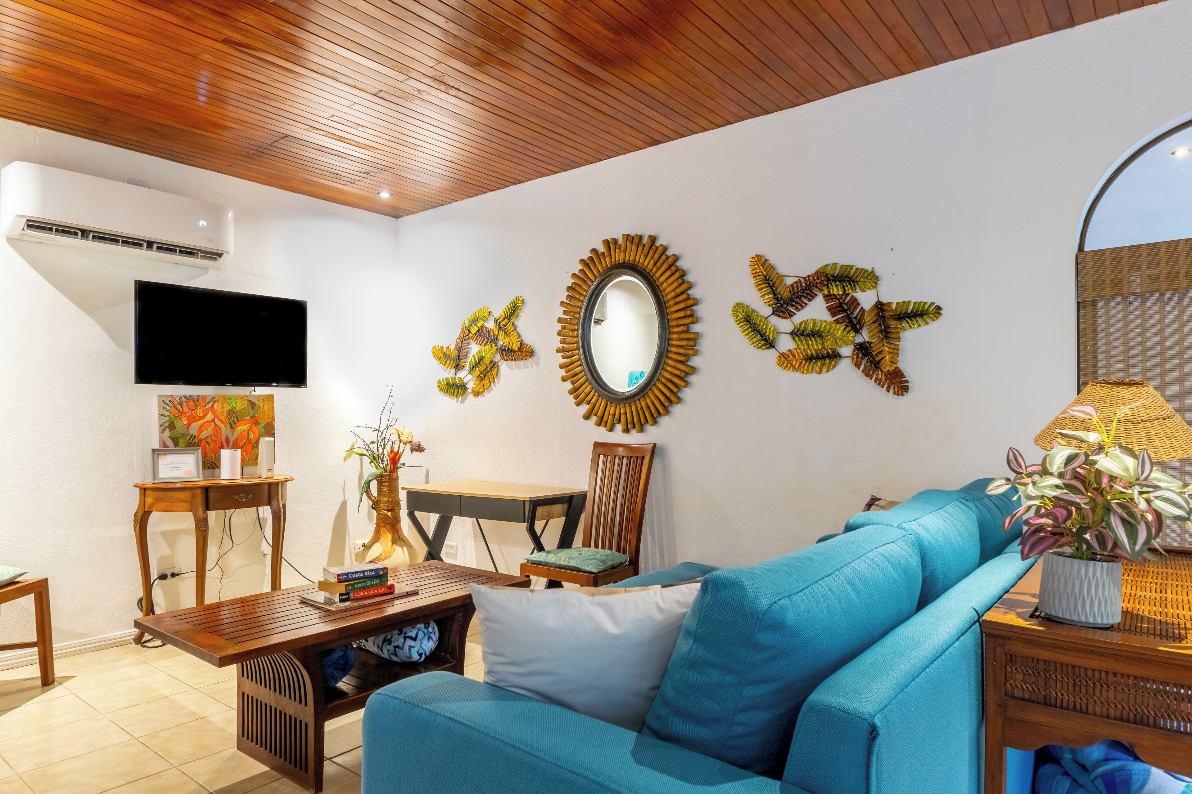 A living room with a blue sofa, wooden coffee table, and a TV mounted on the wall.