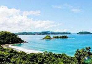 A coastal landscape with a beach, clear blue waters, and lush greenery. - Spacious 2BR/2.5BA Condo in Central Tamarindo CR - Walk to Beach, AC, and Pool (Tamarindo)