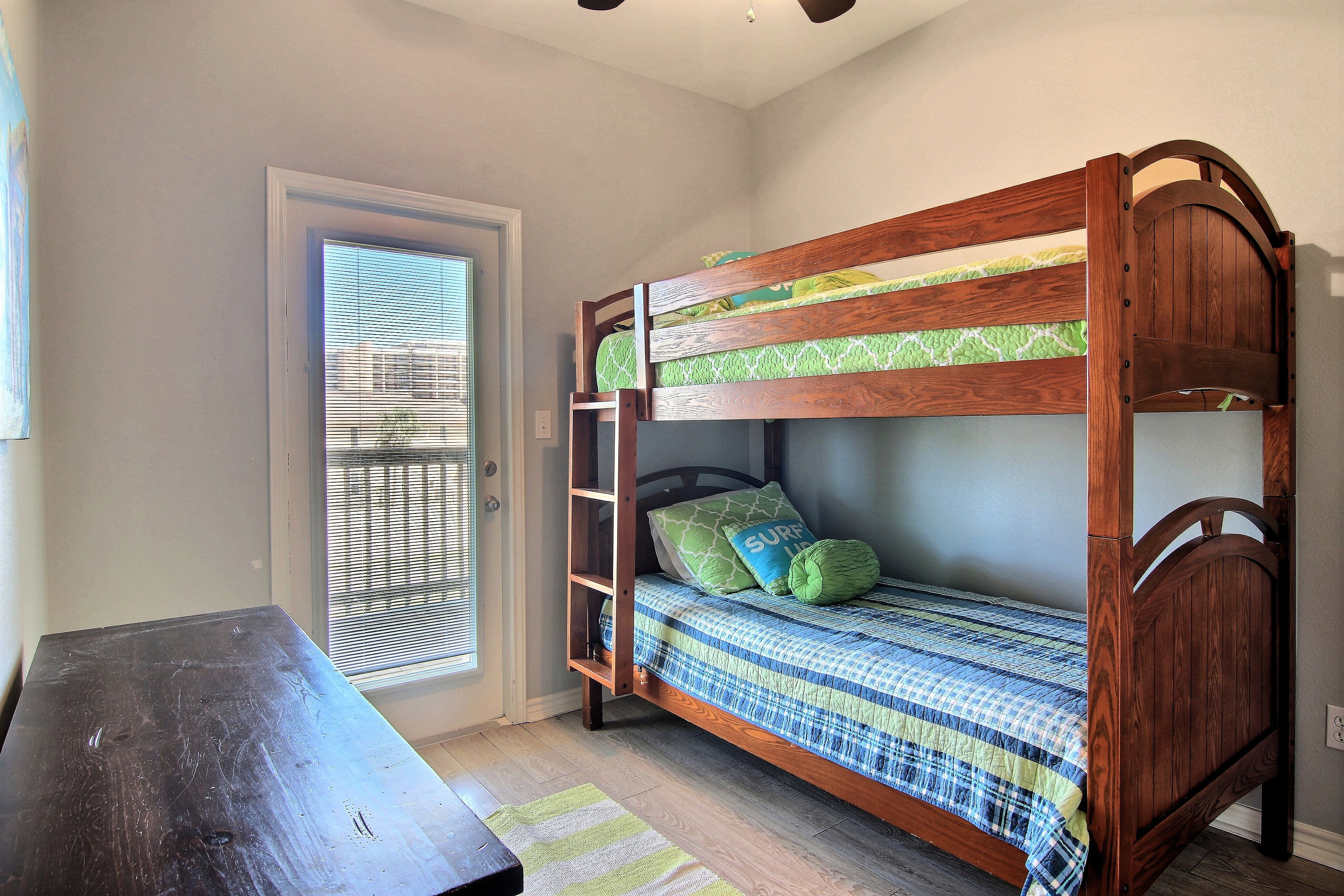 A bunk bed with a ladder, a desk, and a window with blinds.