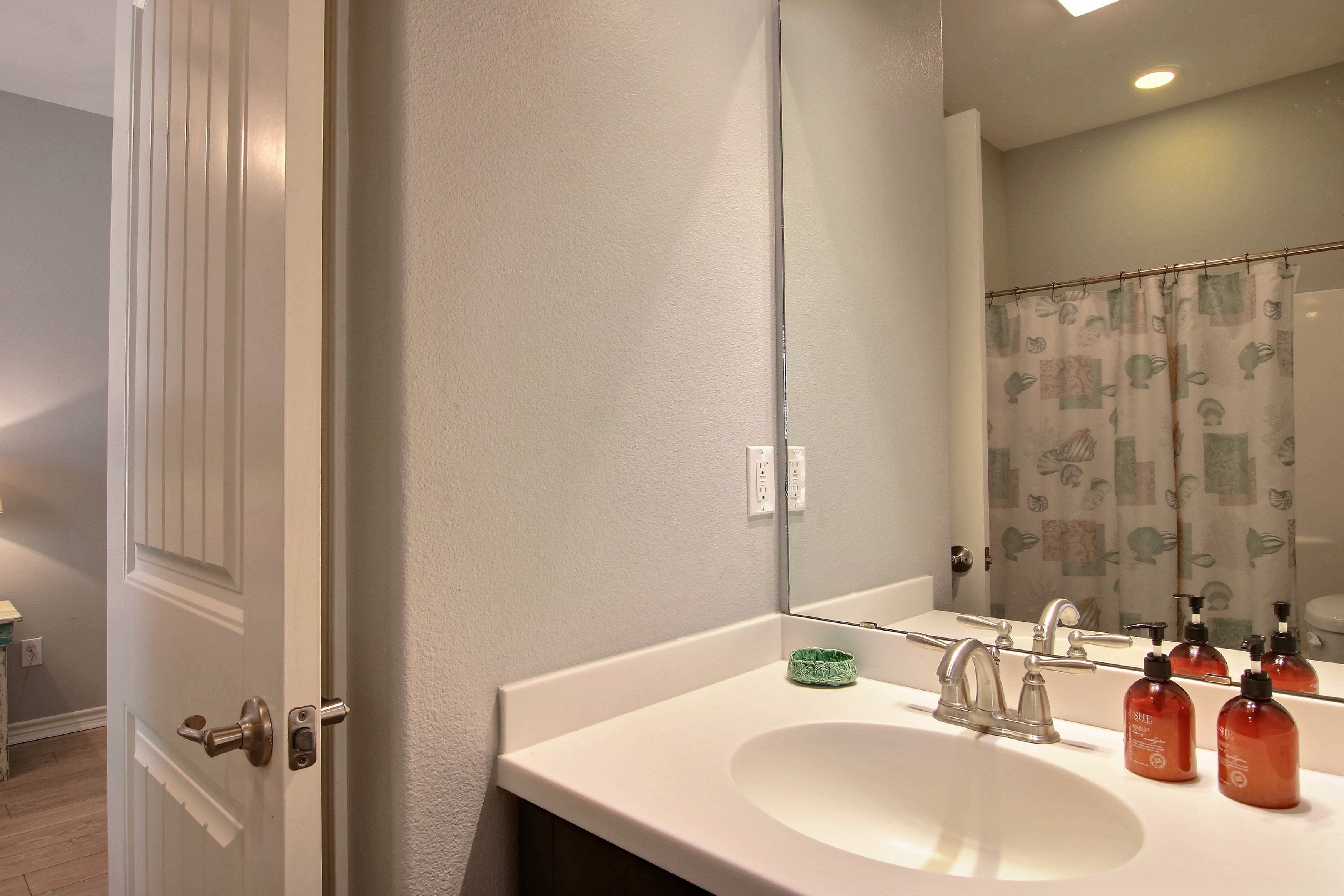 A bathroom with a white sink, a mirror, and a shower curtain with a leaf pattern.