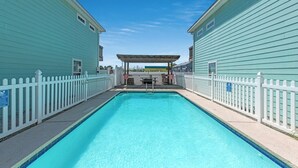 Ein rechteckiger Swimmingpool mit weißen Zäunen an beiden Seiten, ein überdachter Sitzbereich im Hintergrund und ein klarer, blauer Himmel.