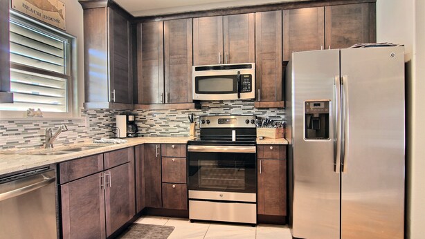 A modern kitchen with dark wood cabinets, stainless steel appliances including a microwave, oven, and refrigerator, and a tiled backsplash. - Family Tides Beach House by Silver Sands Vacation Rentals (Port Aransas)