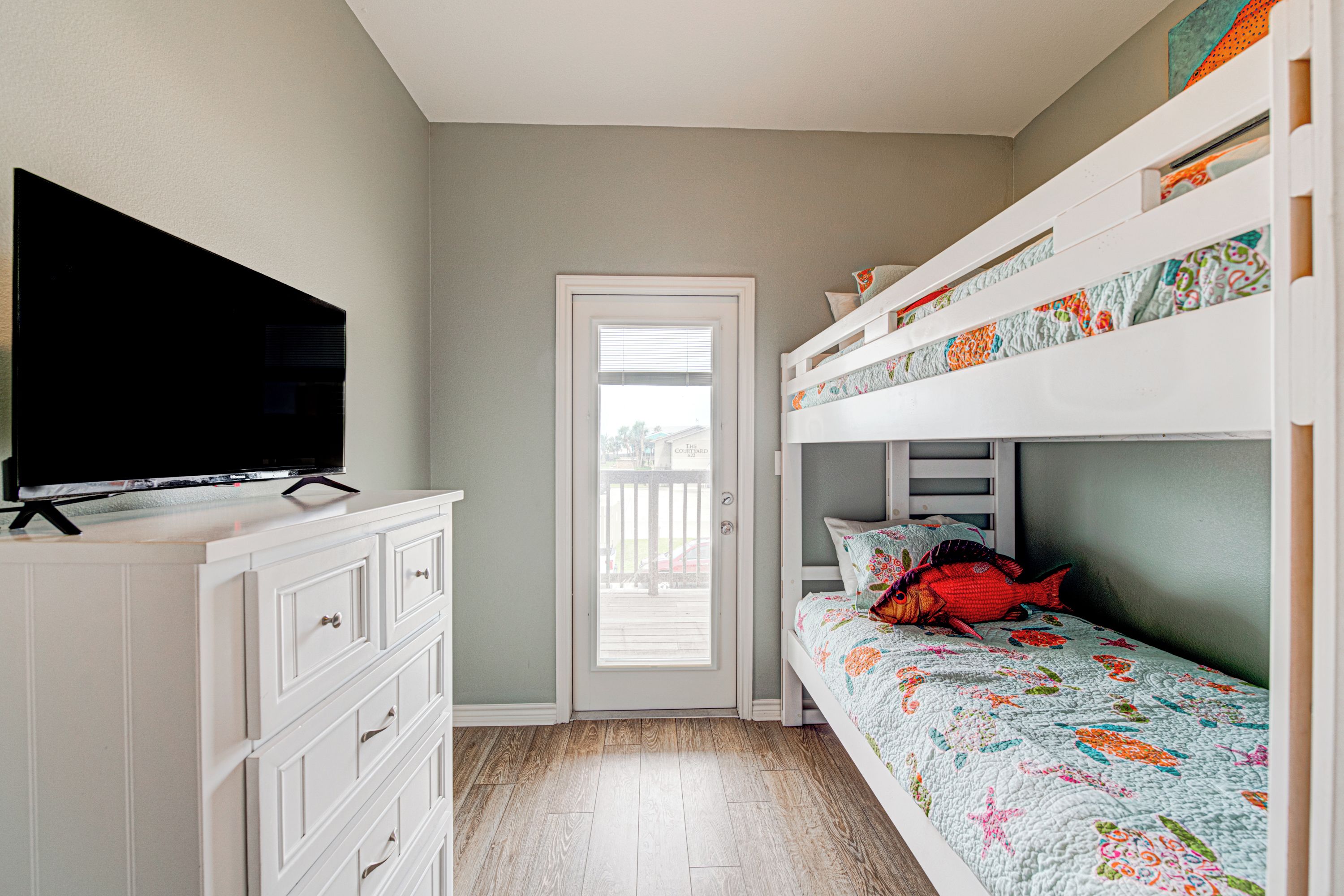 A bedroom with a bunk bed, a TV on a dresser, and a door leading to a balcony.