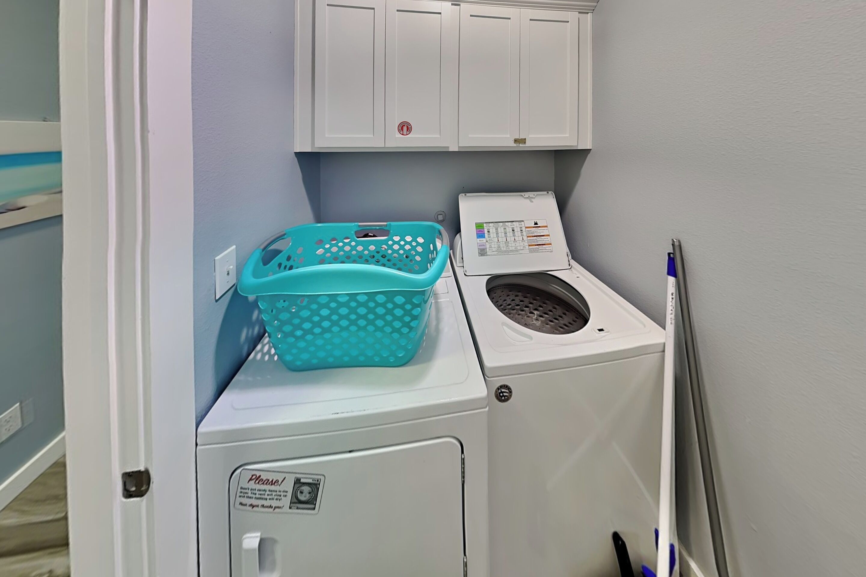 A laundry area with a washing machine, a dryer, a turquoise laundry basket, and a cabinet above the dryer.
