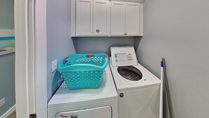 A laundry area with a washing machine, a dryer, a turquoise laundry basket, and a cabinet above the dryer. - Fin And Tonic by Silver Sands Vacation Rentals (Port Aransas)