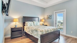 A bedroom with a bed, two nightstands, a TV mounted on the wall, and a door leading to a balcony. - Fin And Tonic by Silver Sands Vacation Rentals (Port Aransas)