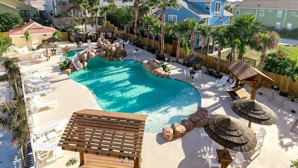 A pool area with lounge chairs, a wooden deck, and palm trees. - Fin And Tonic by Silver Sands Vacation Rentals (Port Aransas)