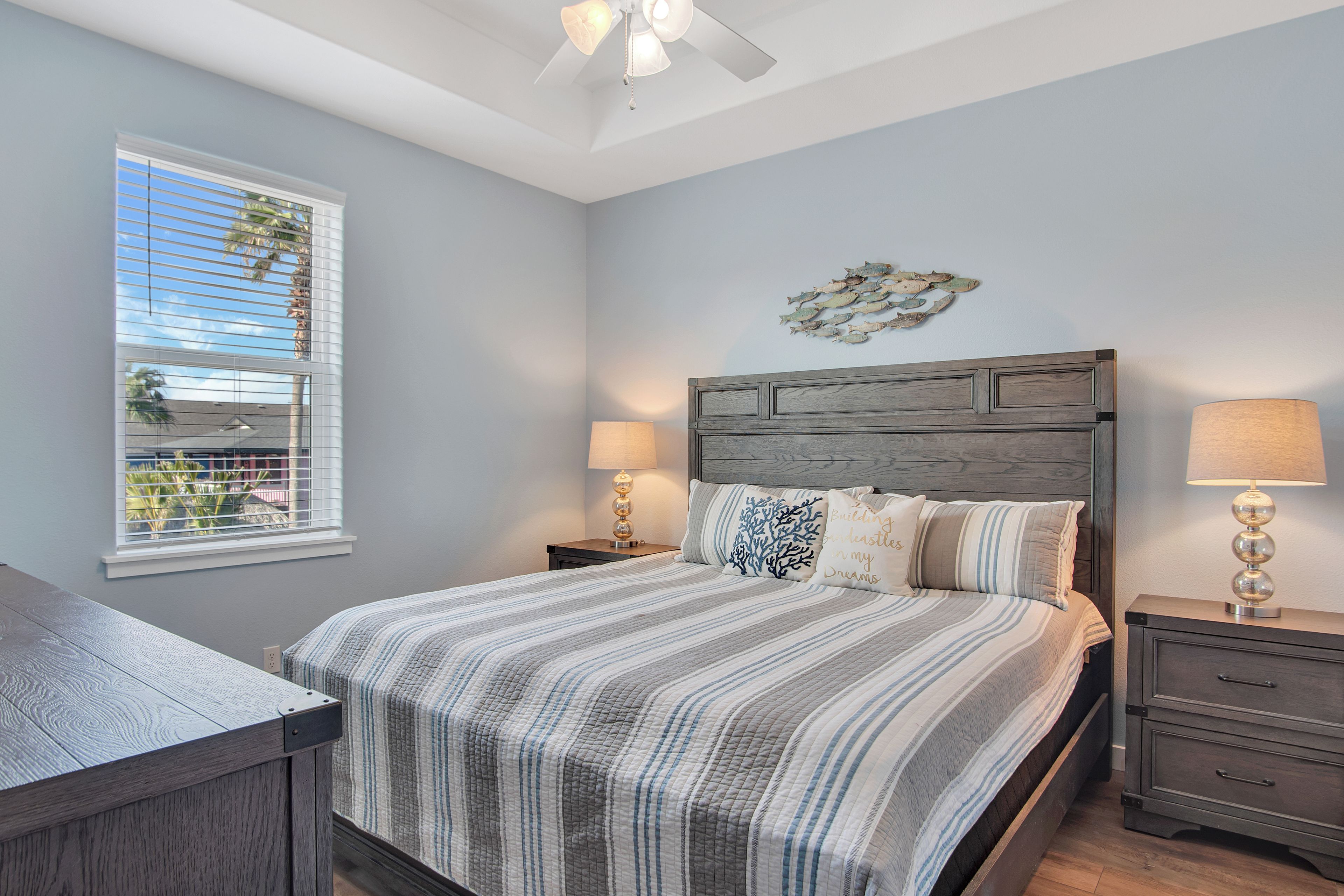 A bedroom with a large bed, two bedside tables, a ceiling fan, and a window with blinds.