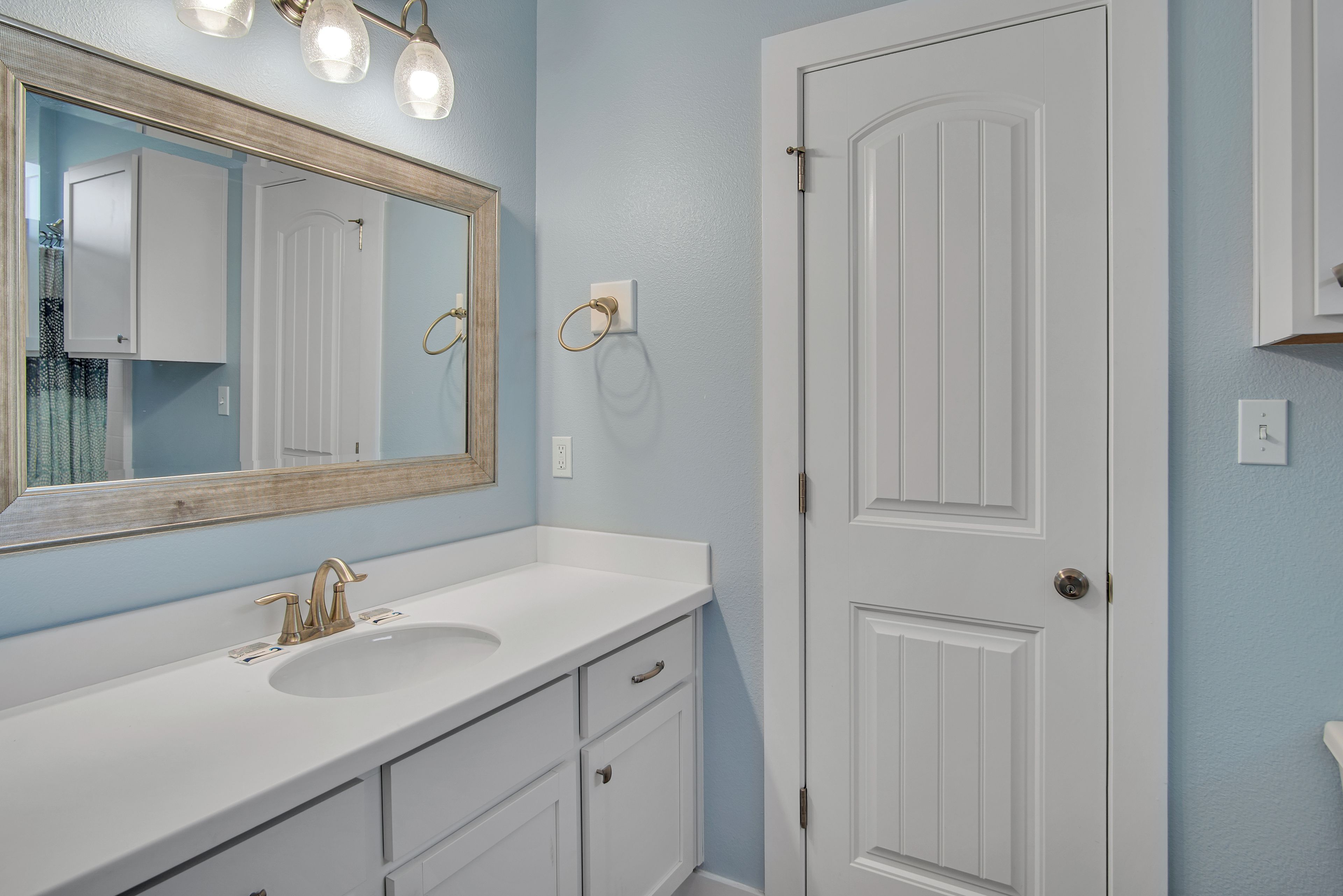 A bathroom with a white vanity, a large mirror, and a door with a handle.