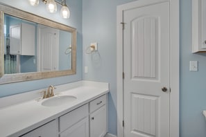 A bathroom with a white vanity, a large mirror, and a white door. - Fin And Tonic by Silver Sands Vacation Rentals (Port Aransas)