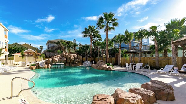 A clear pool with a rock feature, surrounded by lounge chairs and palm trees. - Fin And Tonic by Silver Sands Vacation Rentals (Port Aransas)