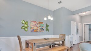 A dining area with a wooden table and benches, a hanging light fixture, and wall art. - Fin And Tonic by Silver Sands Vacation Rentals (Port Aransas)