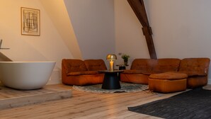 En moderne stue med et stort, hvidt badekar, to brune lædersofaer, et sort sofabord med en lampe og et indrammet abstrakt kunstværk på væggen.