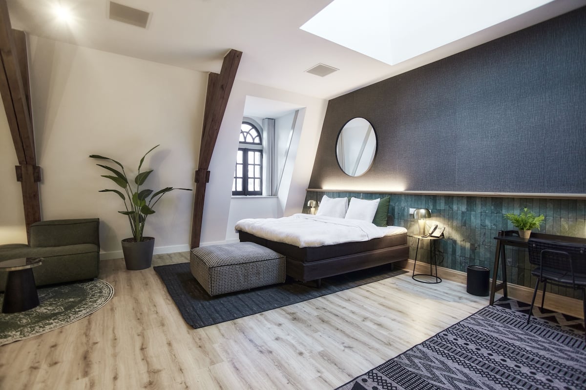 A modern bedroom with a bed, a sofa, a dining table, a potted plant, and a window.