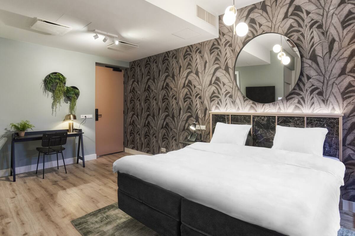A bedroom with a bed, desk, chair, and potted plants.