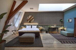 A modern loft bedroom with a skylight, a large bed, a dining area, and a seating area. - Hotel Botanique Breda (Breda)